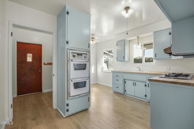 kitchen with light wood finished floors, light countertops, decorative backsplash, double oven, and gas cooktop