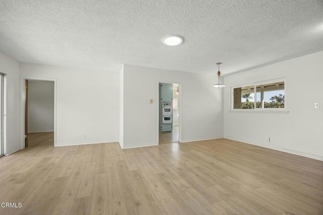 empty room with light wood-type flooring, a textured ceiling, and baseboards