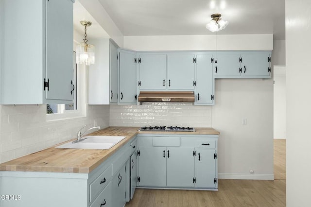 kitchen with stainless steel gas cooktop, light countertops, decorative backsplash, a sink, and under cabinet range hood