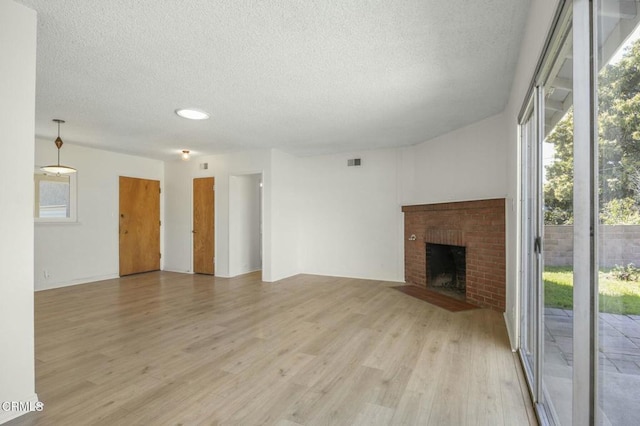 unfurnished living room featuring a textured ceiling, light wood finished floors, a fireplace, and a healthy amount of sunlight