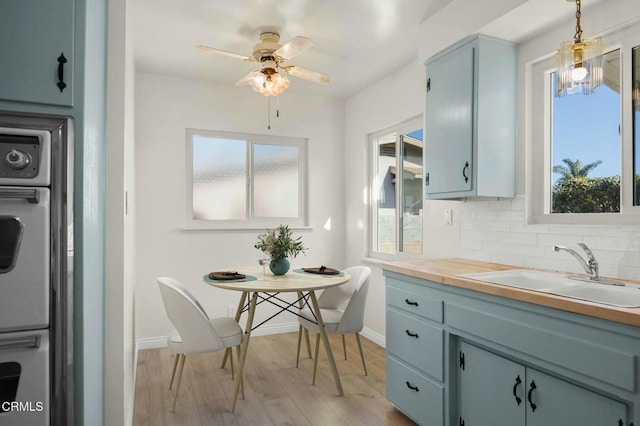 kitchen with light wood finished floors, tasteful backsplash, wall oven, a sink, and baseboards