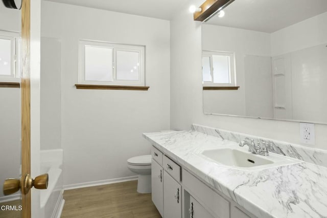 bathroom with a bathtub, toilet, vanity, wood finished floors, and baseboards