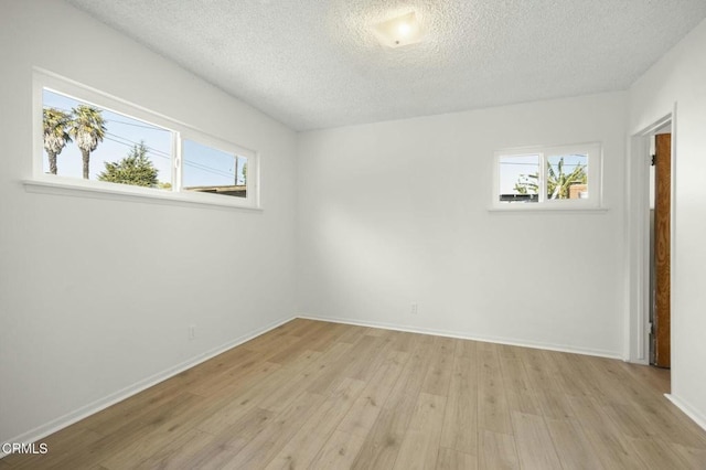 empty room featuring light wood-style floors, a textured ceiling, and baseboards