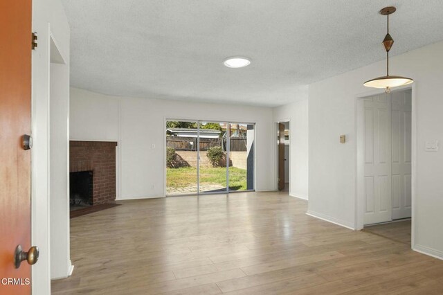 unfurnished living room featuring a brick fireplace, a textured ceiling, baseboards, and wood finished floors