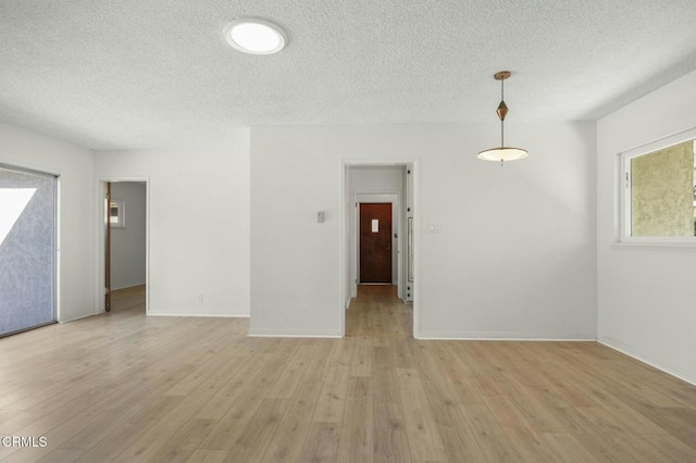 spare room with a textured ceiling, baseboards, and light wood-style floors