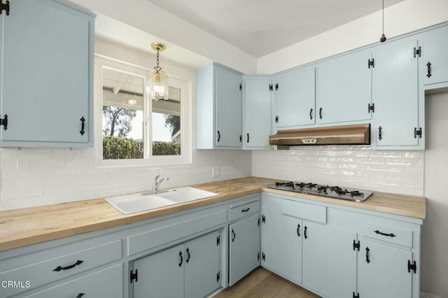 kitchen featuring stainless steel gas cooktop, hanging light fixtures, backsplash, a sink, and under cabinet range hood