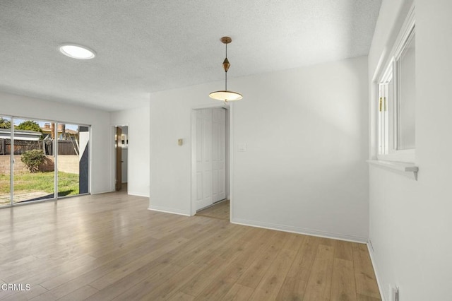 spare room featuring light wood-style flooring, baseboards, and a textured ceiling