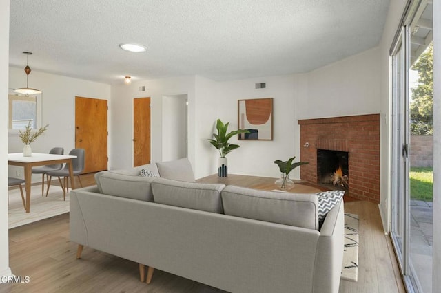 living room featuring a textured ceiling, a fireplace, visible vents, and wood finished floors