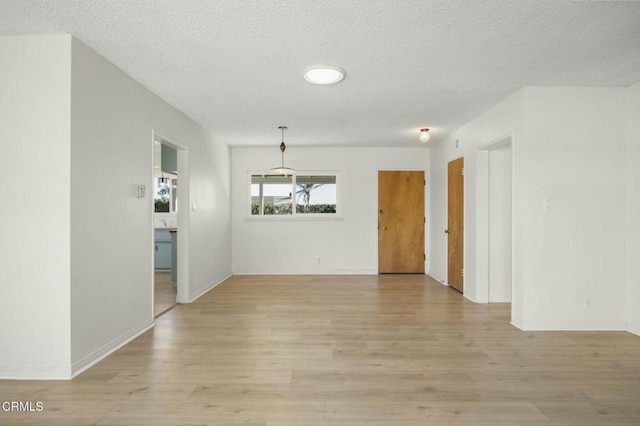 unfurnished room with light wood finished floors, baseboards, and a textured ceiling