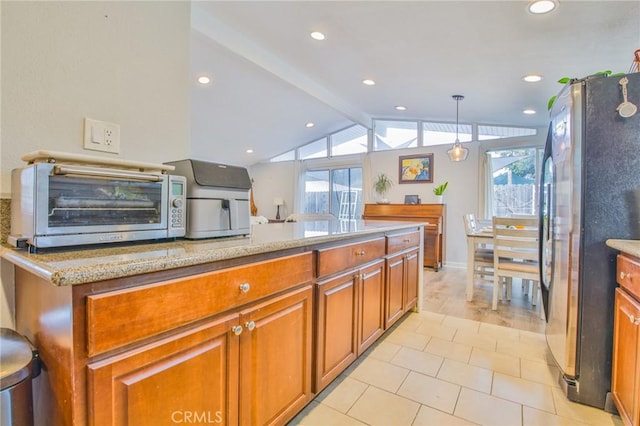 kitchen with lofted ceiling with beams, light stone counters, brown cabinetry, and freestanding refrigerator