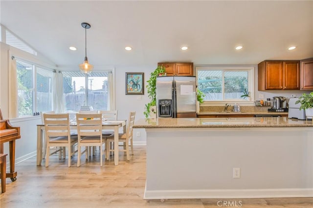 kitchen featuring light wood-style flooring, light stone countertops, stainless steel fridge with ice dispenser, brown cabinets, and decorative light fixtures