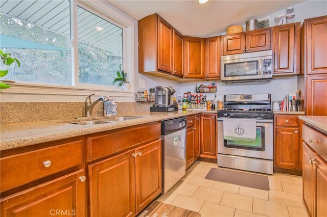 kitchen with appliances with stainless steel finishes, brown cabinetry, light tile patterned flooring, and a sink