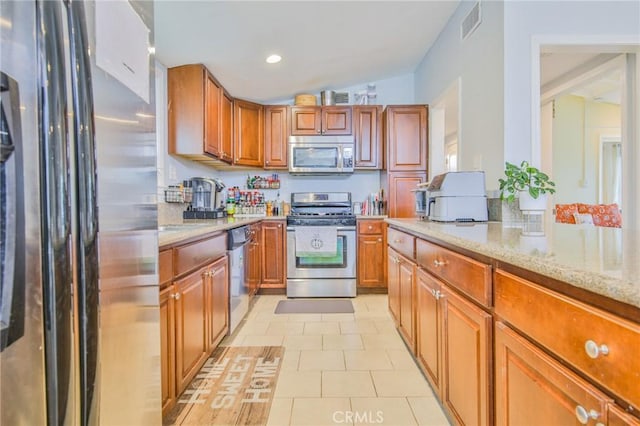 kitchen featuring light stone countertops, appliances with stainless steel finishes, vaulted ceiling, and light tile patterned flooring