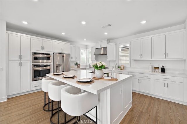 kitchen featuring under cabinet range hood, white cabinetry, appliances with stainless steel finishes, a breakfast bar area, and light countertops