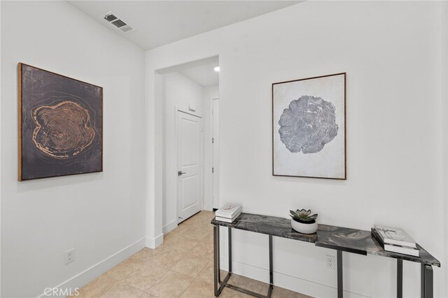 hallway with light tile patterned floors, visible vents, and baseboards