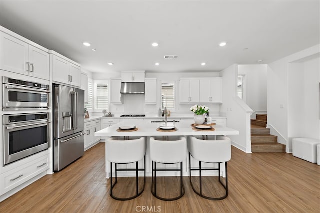 kitchen featuring under cabinet range hood, a kitchen bar, light countertops, stainless steel appliances, and a sink