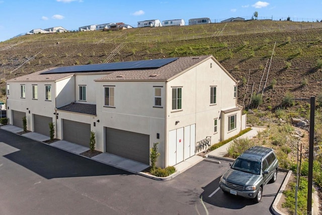 exterior space featuring roof with shingles, roof mounted solar panels, and stucco siding