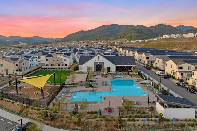 pool at dusk with a residential view, a mountain view, and fence