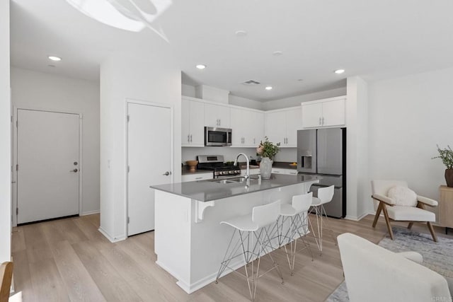 kitchen featuring a breakfast bar, a sink, white cabinets, light wood-style floors, and appliances with stainless steel finishes