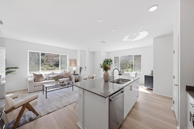 kitchen with light wood-style flooring, open floor plan, stainless steel dishwasher, white cabinetry, and a sink