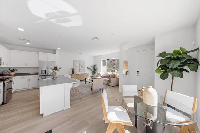 interior space featuring visible vents, an island with sink, light wood-style flooring, appliances with stainless steel finishes, and a sink