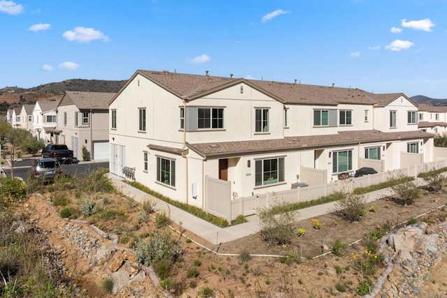 rear view of property featuring a residential view, fence, and stucco siding