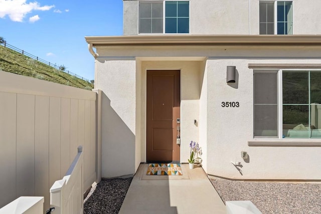 entrance to property featuring fence and stucco siding