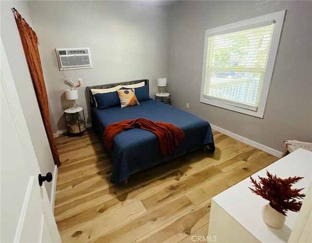 bedroom featuring a wall mounted AC, wood finished floors, and baseboards