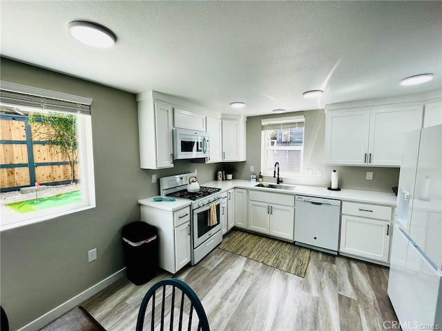 kitchen featuring light wood-type flooring, white appliances, white cabinetry, and a sink