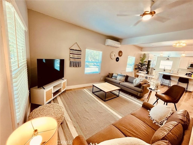 living area featuring baseboards, light wood-style floors, a wall mounted AC, and a healthy amount of sunlight