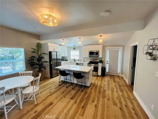 kitchen with appliances with stainless steel finishes, a kitchen breakfast bar, light countertops, light wood-style floors, and white cabinetry