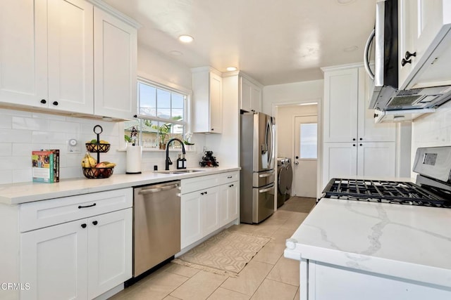 kitchen with decorative backsplash, appliances with stainless steel finishes, white cabinets, a sink, and washer and dryer