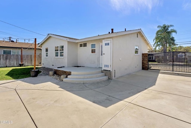 rear view of house with a yard, a patio, stucco siding, a gate, and fence