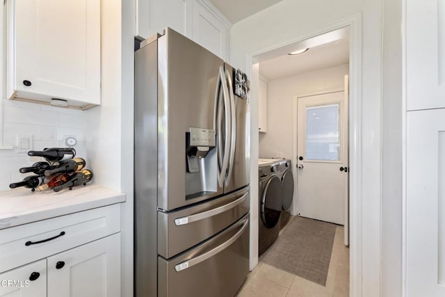 kitchen featuring washing machine and dryer, white cabinets, stainless steel fridge, and backsplash