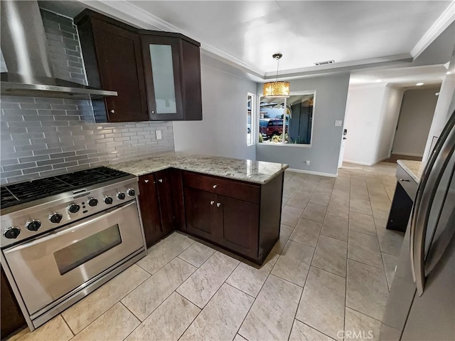 kitchen featuring dark brown cabinetry, wall chimney range hood, appliances with stainless steel finishes, decorative backsplash, and crown molding