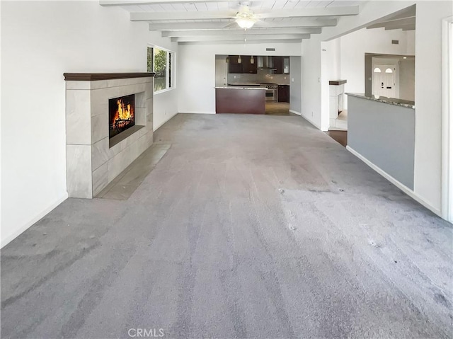 unfurnished living room with a ceiling fan, a fireplace, beam ceiling, and baseboards
