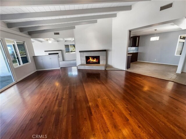 unfurnished living room featuring a ceiling fan, visible vents, a tiled fireplace, and wood finished floors