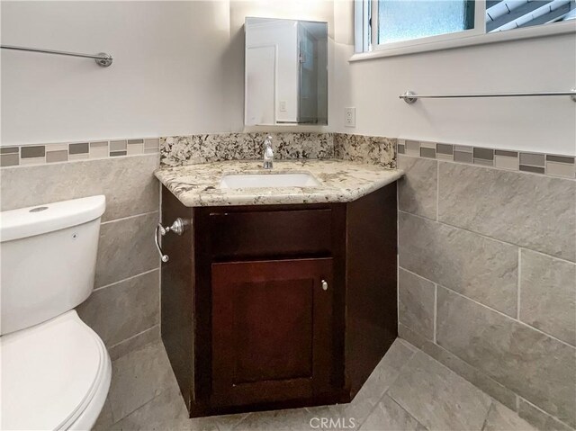 bathroom featuring a wainscoted wall, tile walls, toilet, and vanity