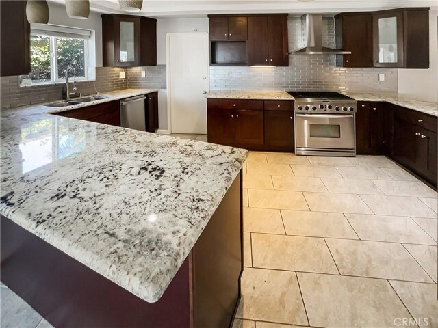 kitchen with stainless steel appliances, backsplash, a sink, wall chimney range hood, and light stone countertops