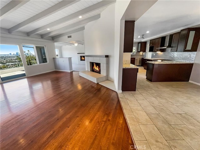 unfurnished living room featuring baseboards, a tiled fireplace, vaulted ceiling with beams, light wood-style floors, and recessed lighting