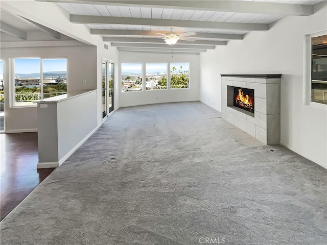 unfurnished living room featuring wood ceiling, beamed ceiling, a tiled fireplace, and a wealth of natural light