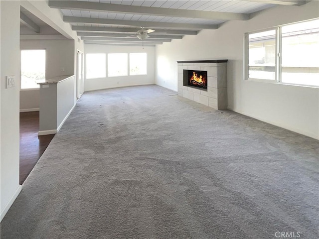 unfurnished living room featuring beamed ceiling, carpet flooring, a tile fireplace, and a ceiling fan