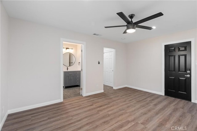 unfurnished bedroom featuring ensuite bath, visible vents, baseboards, and wood finished floors