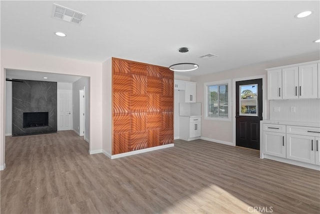 unfurnished living room featuring light wood-style flooring, a premium fireplace, visible vents, and baseboards