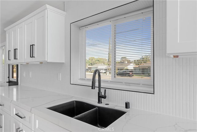 kitchen with light stone countertops, white cabinets, and a sink