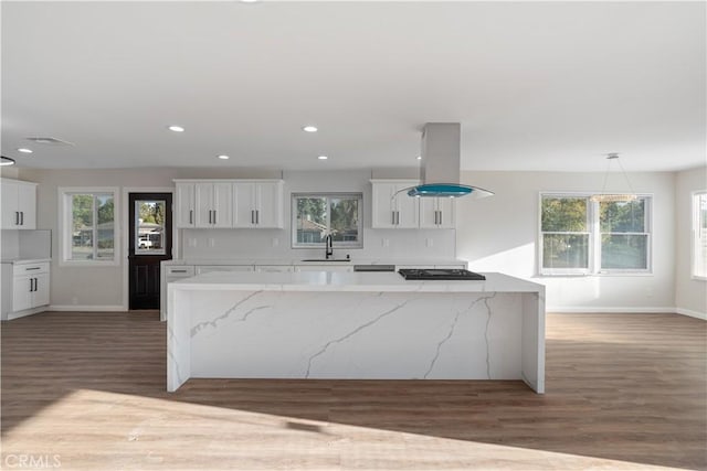 kitchen featuring a spacious island, island range hood, white cabinets, and a sink