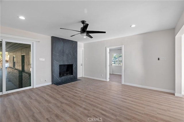 unfurnished living room with baseboards, wood finished floors, a high end fireplace, and a ceiling fan