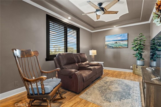 living room featuring a raised ceiling, ceiling fan, baseboards, and wood finished floors