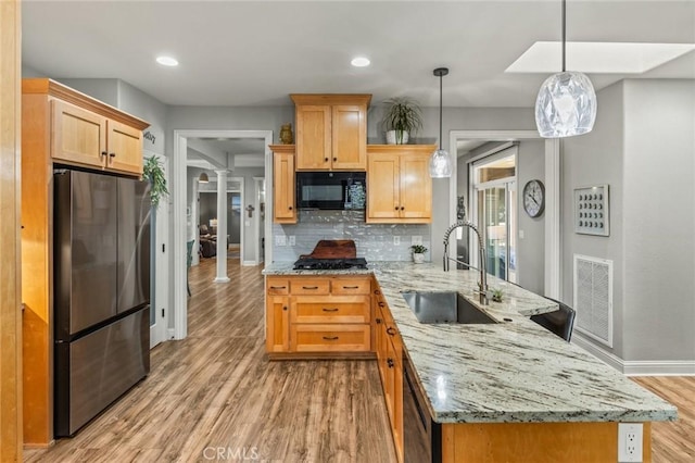 kitchen with visible vents, freestanding refrigerator, light brown cabinets, black microwave, and a sink