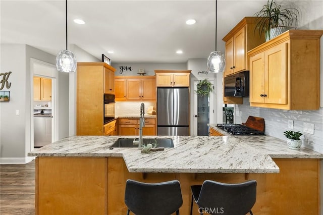 kitchen featuring a peninsula, black appliances, light stone counters, and a sink